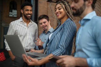 Cheerful young businesspeople with laptop working in office, social inclusion and cooperation concept.