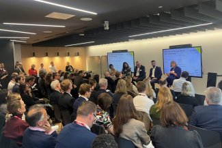 Numerous individuals sitting together in a spacious room, participating in a discussion or meeting.