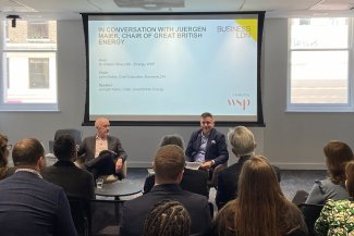 Attendees sitting in a conference room, engaged in a conversation between Juergen Maier and John Dickie, with visual aids displayed, featuring speakers names and logos for BusinessLDN and WSP.