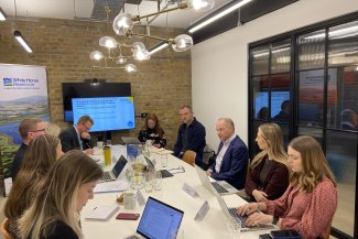  A team of people gathered around a table, each with a laptop, actively participating in a group discussion.