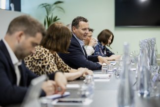 A diverse group of people seated at a long table, engaged in conversation during a roundtable.