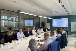A group of people engaged in discussion while seated at a long table in a meeting room.