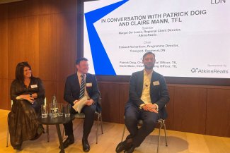 Three individuals seated on chairs. Behind them, a large screen event title, with BusinessLDN branding and Atkins Realis logo as sponsor.