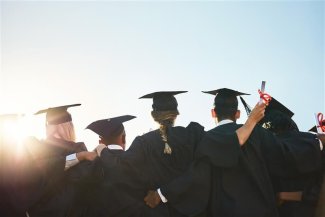 Graduates in black gowns standing in a line, celebrating their academic achievements at a graduation ceremony.