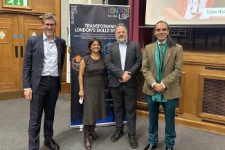 Four individuals standing together in front of a large LSIP banner, smiling and posing for the camera