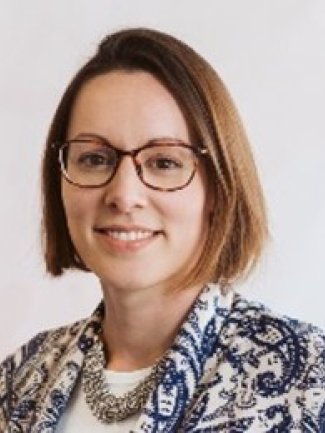 A woman wearing glasses and a blue and white jacket smiles at the camera.