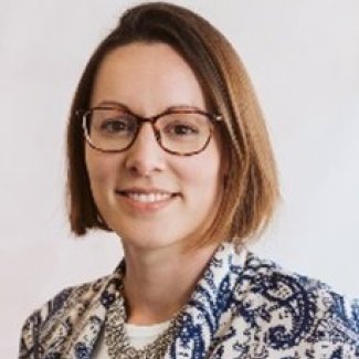 A woman wearing glasses and a blue and white jacket smiles at the camera.